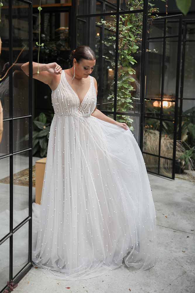 Studio Levana Allium wedding dress featuring a romantic A-line silhouette with cascading tulle, pearl accents, and sheer bell sleeves