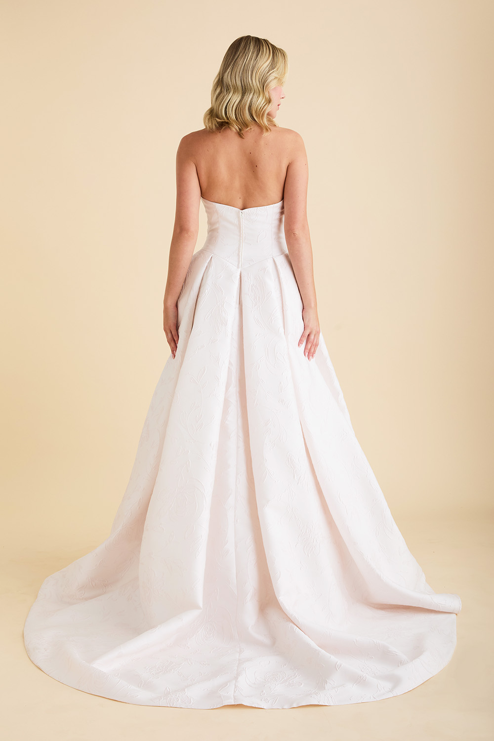 Ivory strapless Astrid & Mercedes Echo wedding dress featuring a Basque waistline, straight-across neckline, angled bodice seams, full jacquard skirt with inverted box pleats, and chapel train