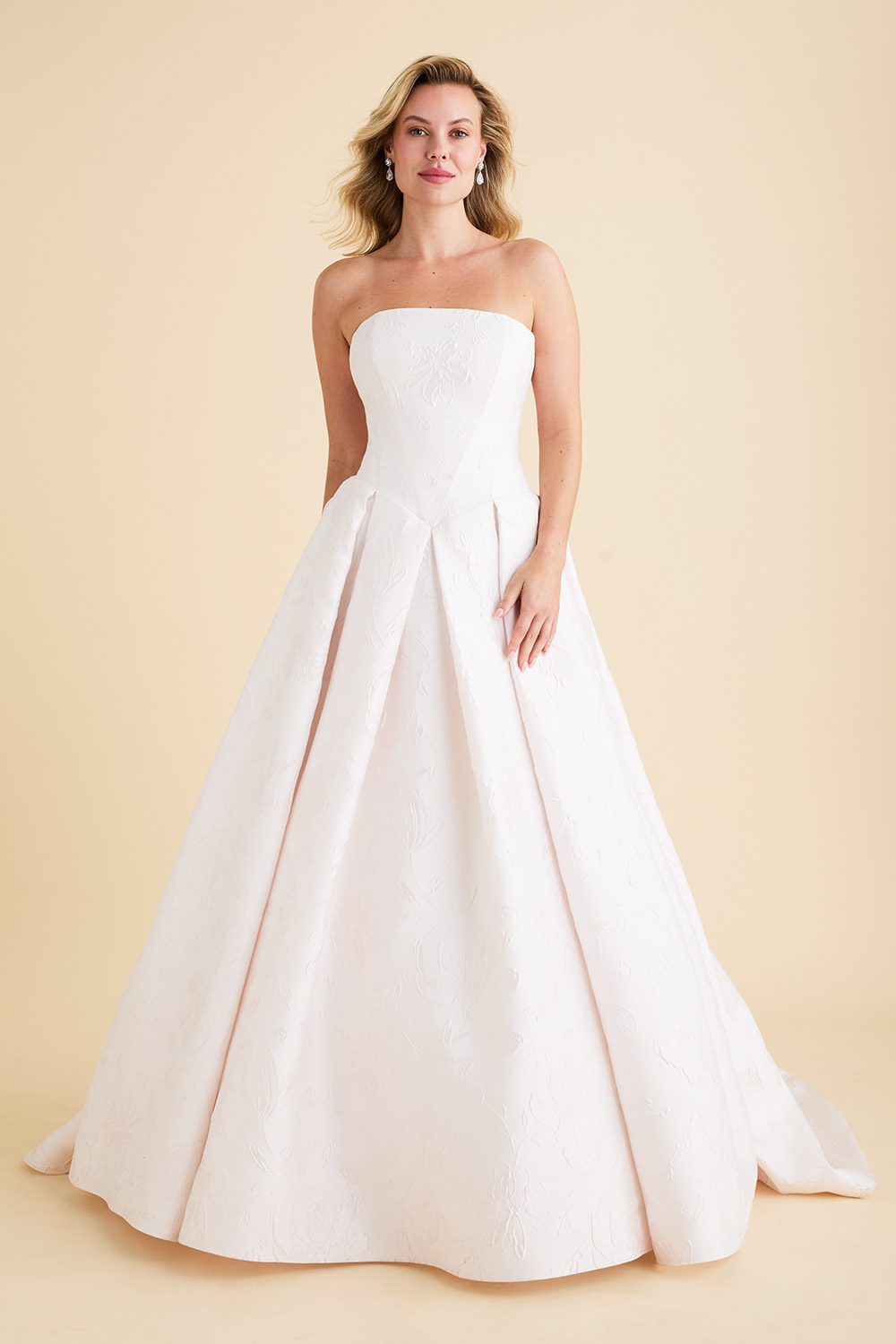 Ivory strapless Astrid & Mercedes Echo wedding dress featuring a Basque waistline, straight-across neckline, angled bodice seams, full jacquard skirt with inverted box pleats, and chapel train