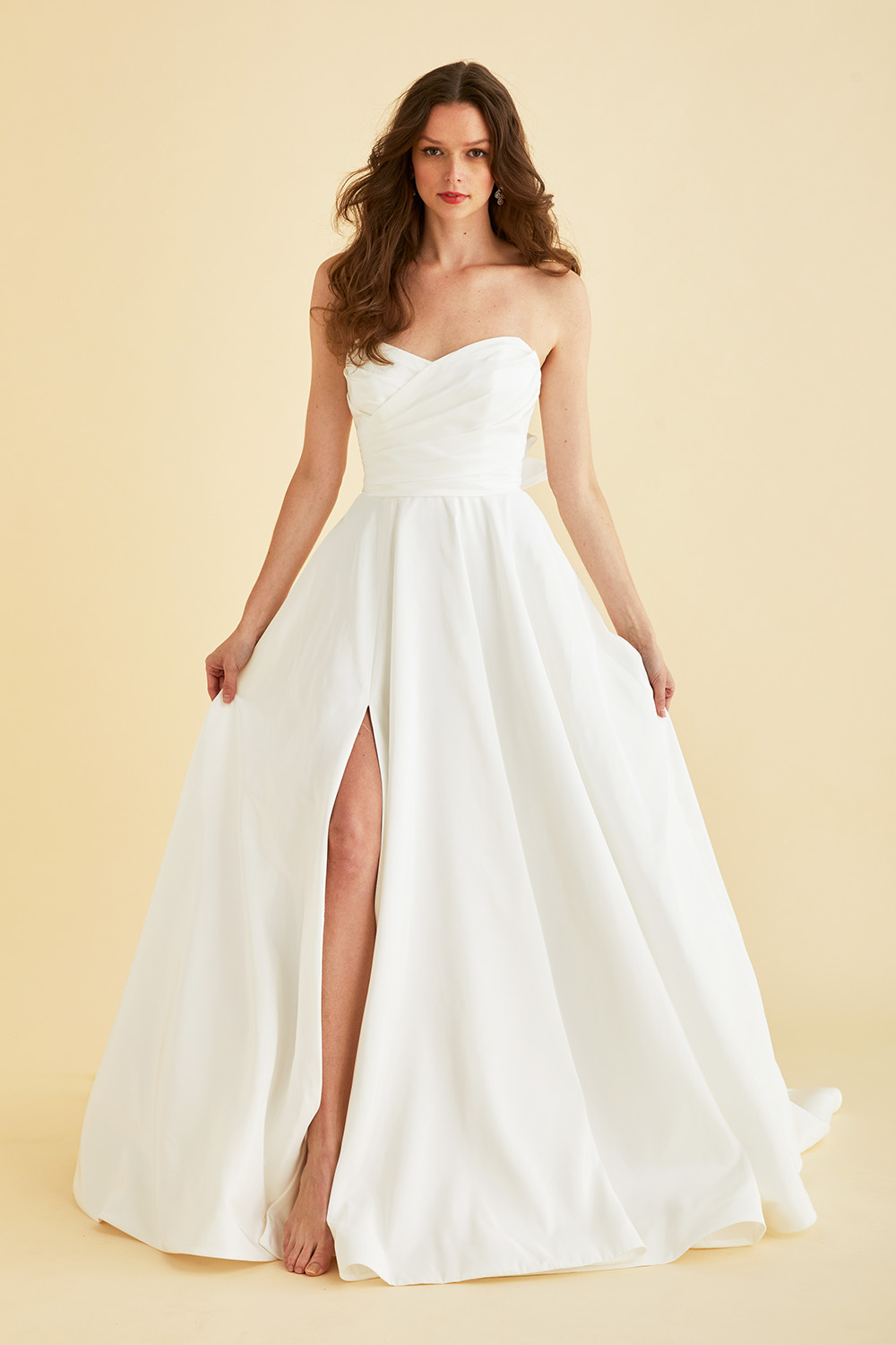 Ivory Astrid & Mercedes Jewel wedding gown—sweetheart ruched bodice, A‑line full circle taffeta skirt with pockets, thigh‑high slit, and vertical statement back bow