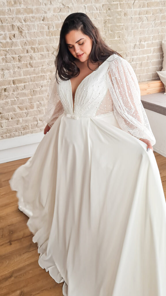 Studio Levana Meagan wedding dress with plunging neckline, nude lining, lace overlay, and hidden pockets