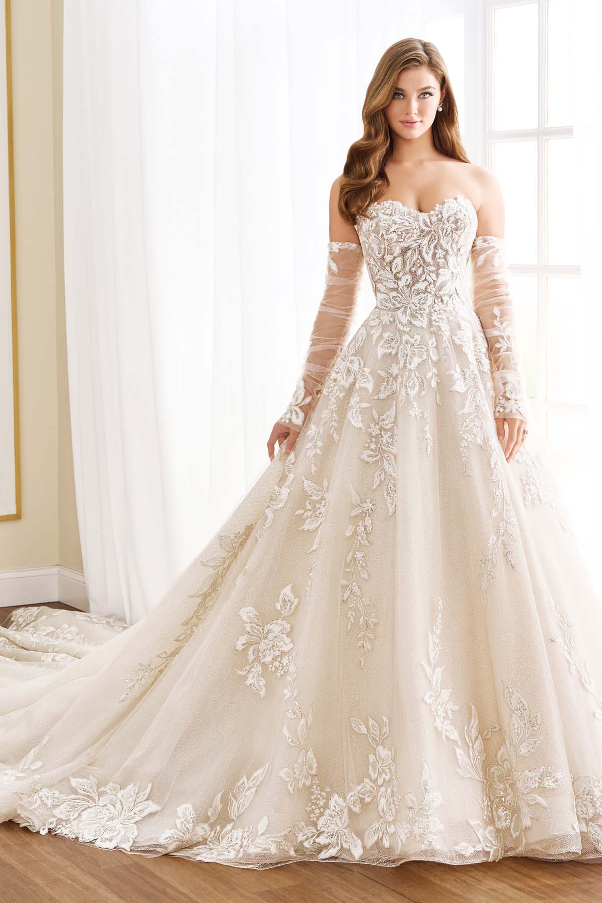 Ivory Martin Thornburg Amaryllis MT9102 ball gown with sweetheart strapless neckline, floral lace appliqués, shimmering glitter net, dropped waist, cathedral train, and detachable illusion long sleeves