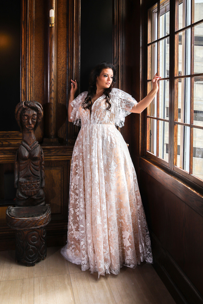 Nera wedding dress by Studio Levana featuring a sequin lace bodice, deep V-neckline, pleated A-line skirt, and detachable illusion sleeves