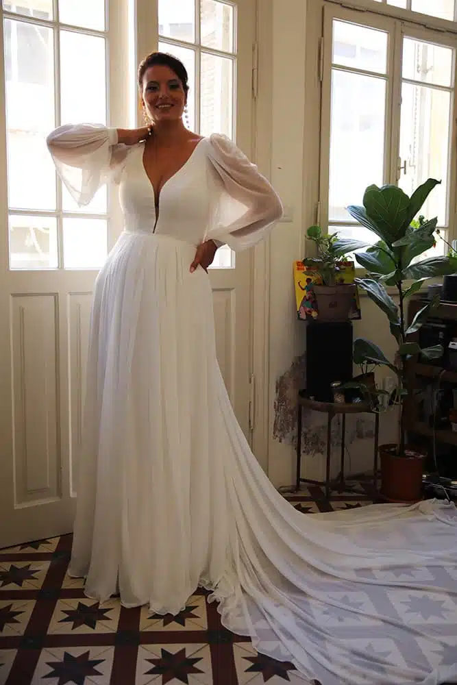 London Sunset wedding dress by Studio Levana featuring sheer bishop sleeves, V-neckline, and flowing A-line skirt with train